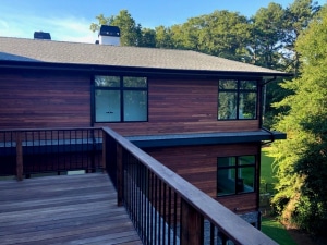 Tigerwood rainscreen siding installed on a modern home exterior with horizontal hardwood cladding, black-framed windows, and an elevated deck overlooking a landscaped backyard.