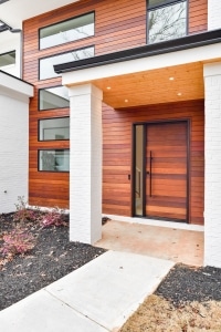Modern home exterior with massaranduba rainscreen siding and matching wood front door, featuring horizontal hardwood cladding, white brick columns, and contemporary black-framed windows.