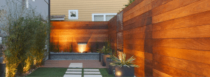 Modern outdoor courtyard featuring a horizontal ipe wood privacy fence wall with integrated landscape lighting and contemporary planters.