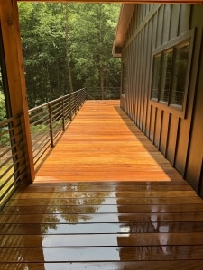 Freshly cleaned and brightened garapa deck with natural golden tones restored, shown before oiling on a covered outdoor balcony surrounded by forest