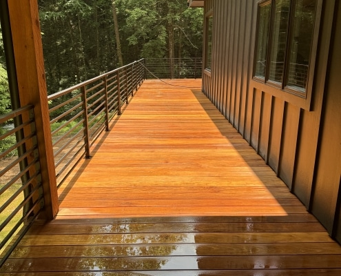 Freshly cleaned and brightened garapa deck with natural golden tones restored, shown before oiling on a covered outdoor balcony surrounded by forest