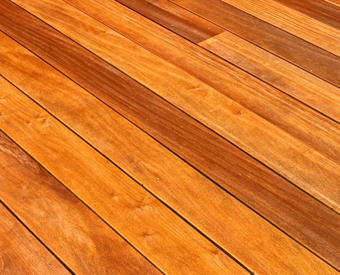 Close up of garapa hardwood decking boards highlighting natural golden color variation and tight straight grain pattern.