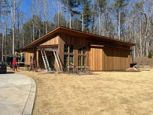 Brown Balau Rainscreen Siding on Modern Residential Build Modern single-story home under construction featuring brown balau rainscreen siding with horizontal wood cladding, large windows, and a low-sloped roof surrounded by tall trees.