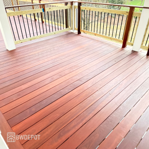 Freshly oiled massaranduba deck boards with rich reddish-brown tones and smooth grain, installed on a covered porch with wood railing and black balusters.