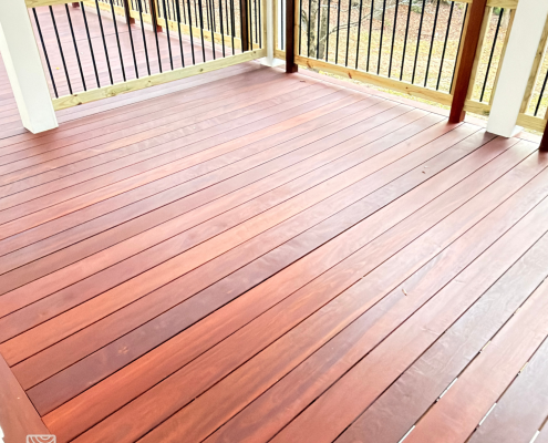 Freshly oiled massaranduba deck boards with rich reddish-brown tones and smooth grain, installed on a covered porch with wood railing and black balusters.