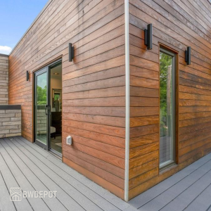 Close-up view of a modern home corner clad in horizontal Ipe siding with black wall sconces and large glass doors.