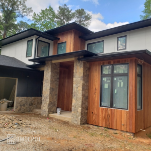 Modern house with Tigerwood wood accent siding around the entry and windows, paired with stone columns and black rooflines.